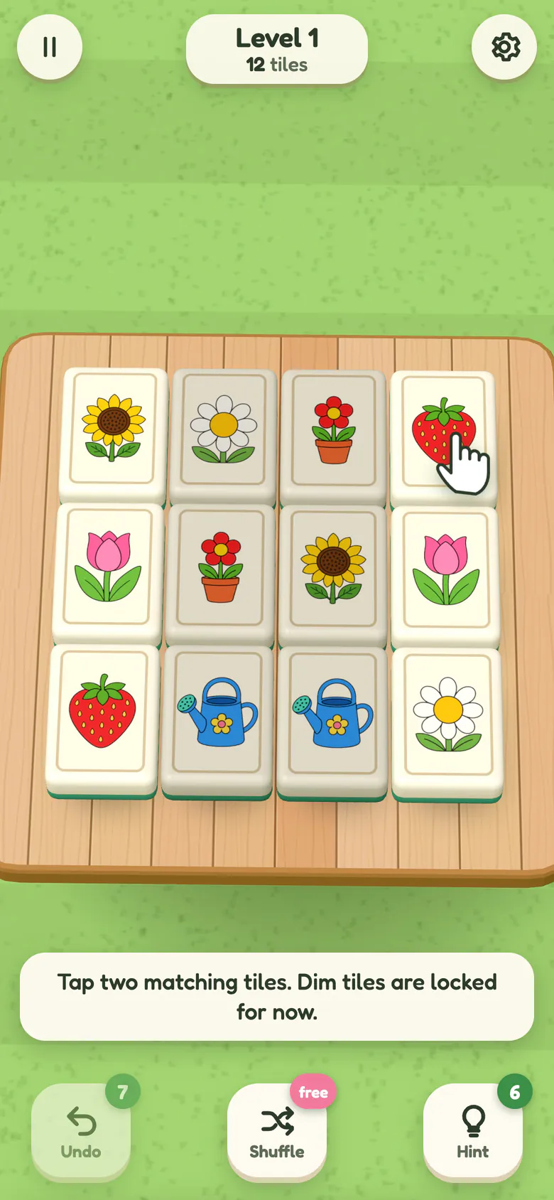 Level 1: twelve big picture tiles on a wooden garden table, a pointing hand on a free strawberry tile and the hint Tap two matching tiles. Dim tiles are locked for now.