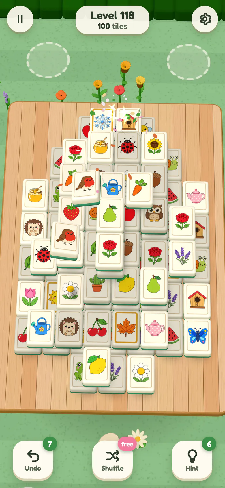 Level 118: a big board of chunky picture tiles stacked five layers high on the garden table; a pair of robin tiles lifts off to be matched, petals sparkle from the last pair and flowers bloom on the lawn behind.